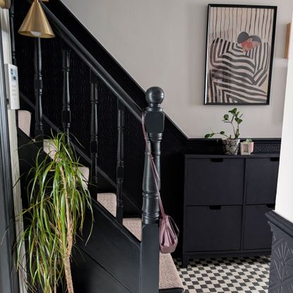 Hallway with lower half of walls painted blue-black, and top half white. Matching blue-black banisters. Black and white chequered flooring