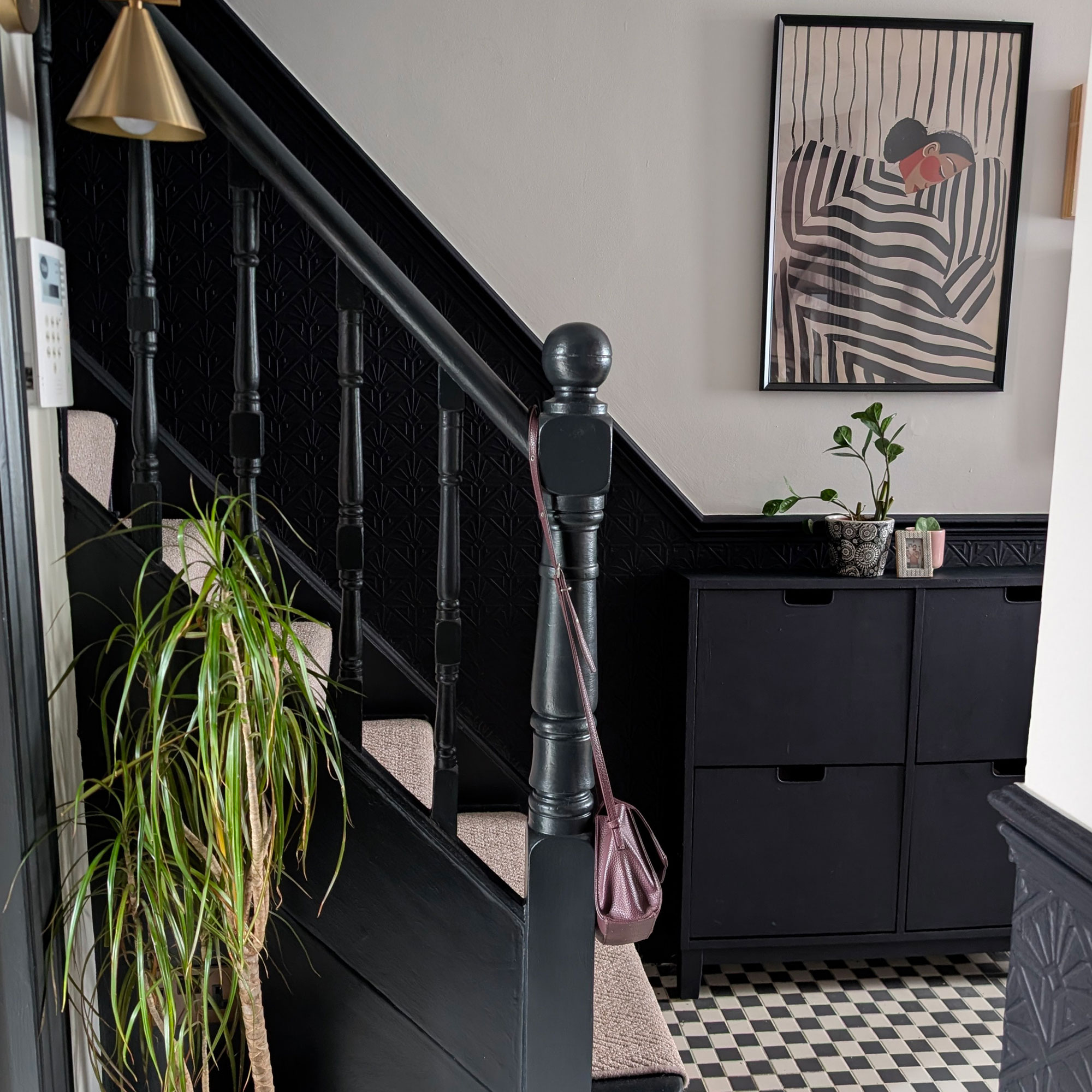 Hallway with lower half of walls painted blue-black, and top half white. Matching blue-black banisters. Black and white chequered flooring