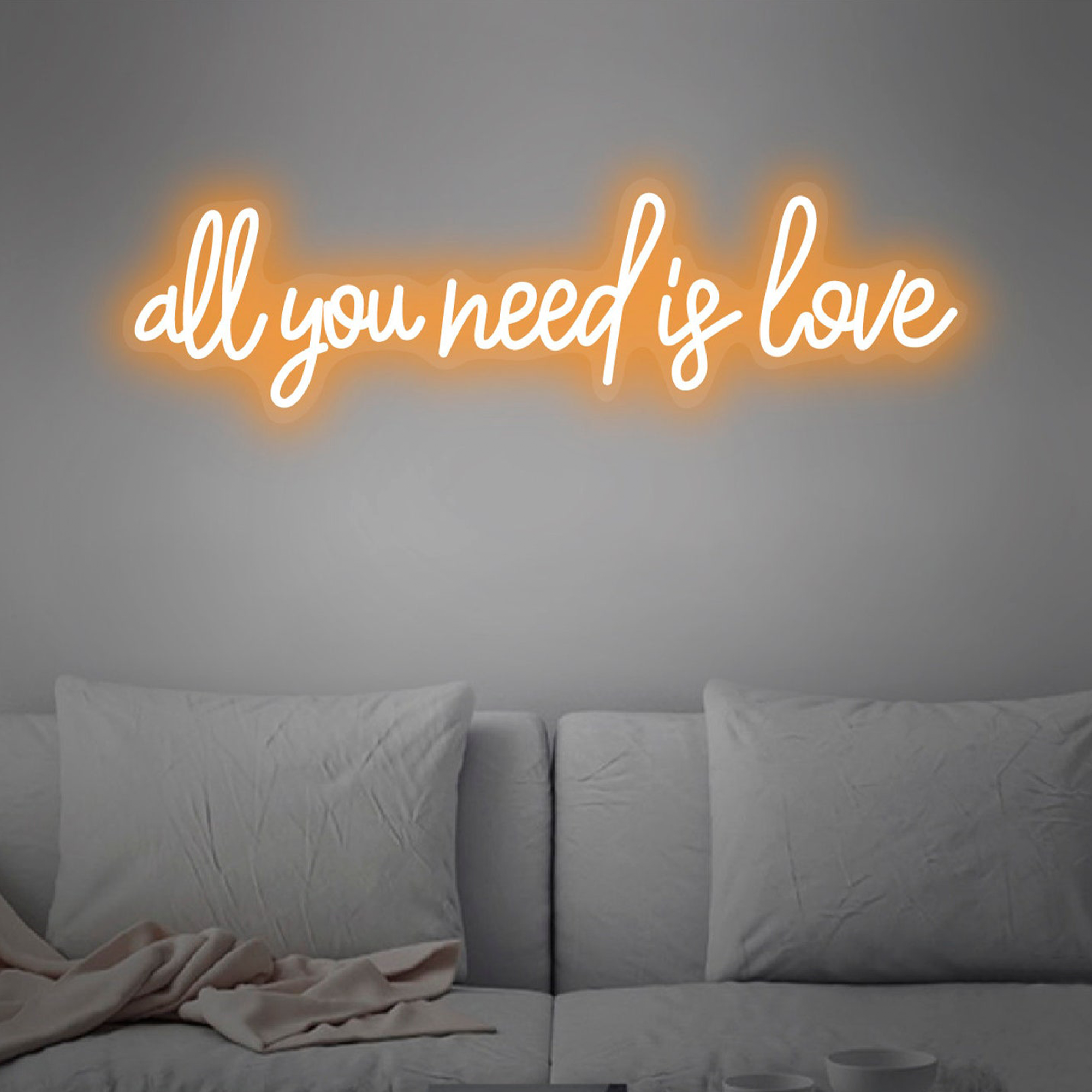 A warm neon sign reading "all you need is love" in a neutral bedroom