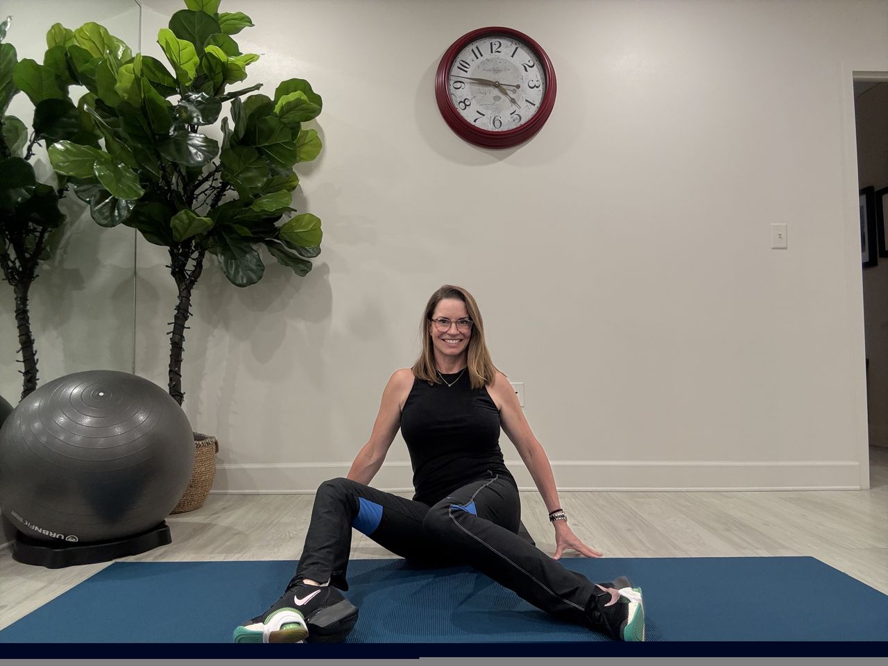 An employe at Femina physical therapy performs windshield wipers, sitting on the floor, hands behind her, dropping her knees to one side.