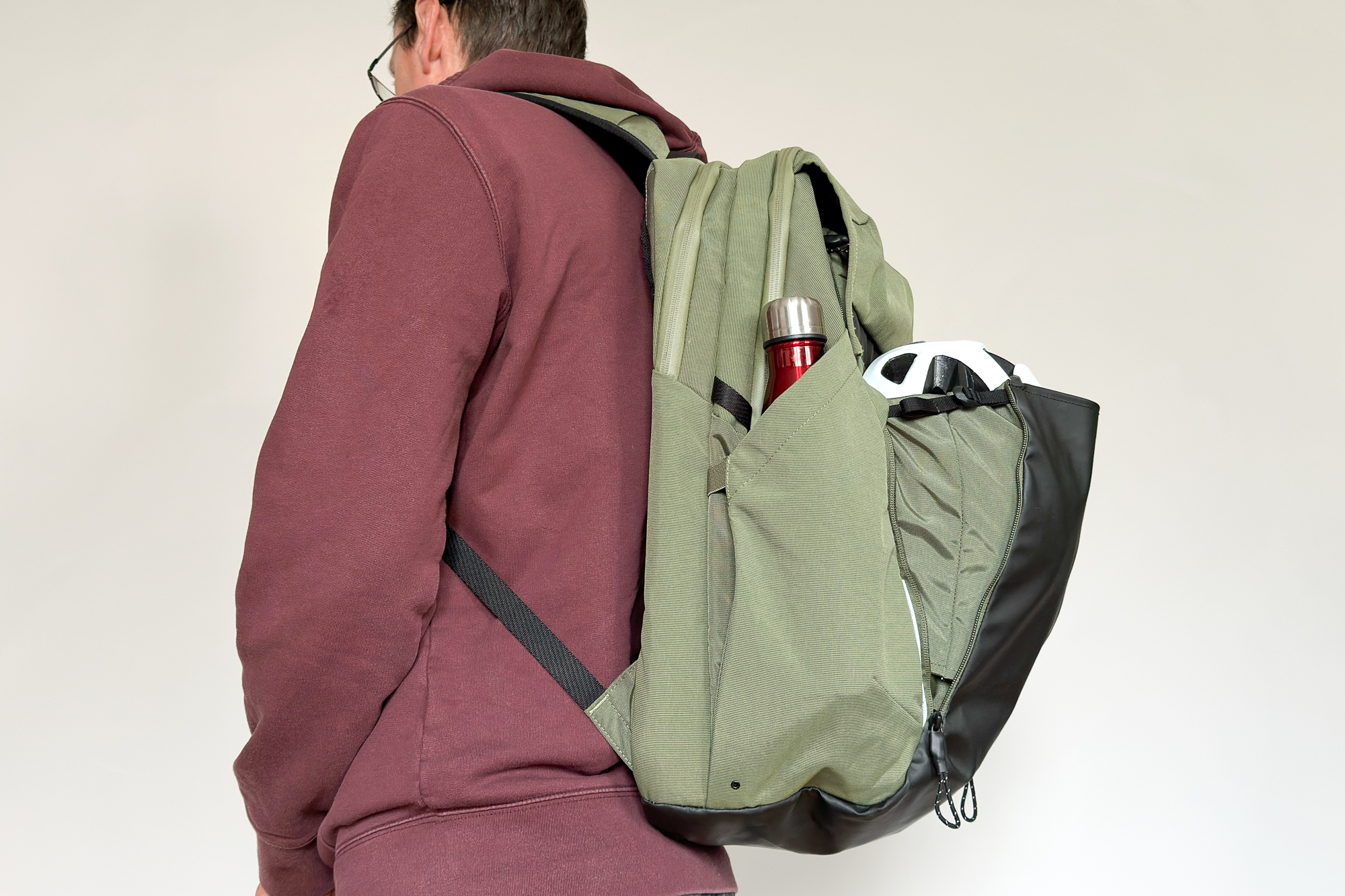 man wearing a green rucksack with a helmet and water bottle in outside pockets