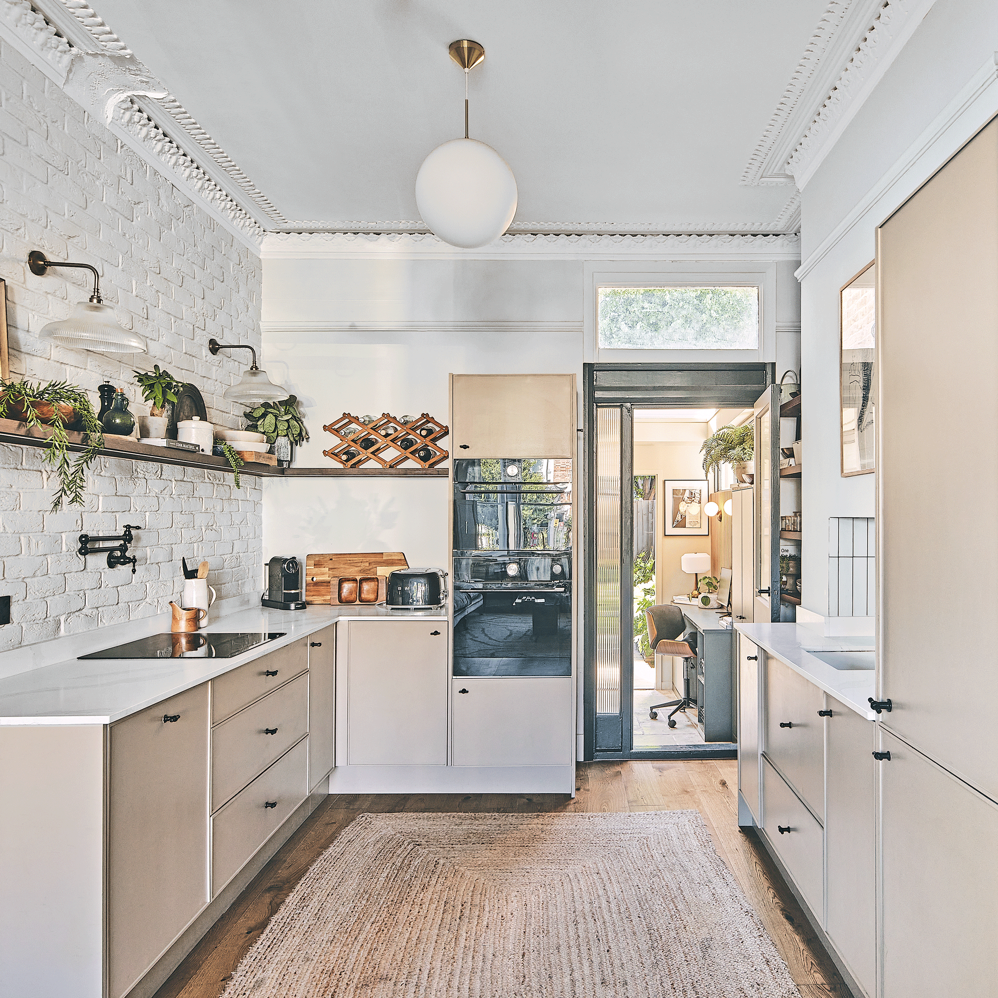 a kitchen with white painted exposed brick walls and beige modern cabinets and an induction hob with open shelving above it
