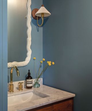 powder room with blue walls, white wall sconce, marble sink and dresser