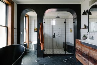 A large bathroom with a walk in shower and freestanding bath, black floor tiles and white wall tiles