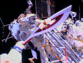 The Olympic torch is seen from the helmet camera of Russian cosmonaut Oleg Kotov in this view from a spacewalk on Nov. 9, 2013. Cosmonaut Sergey Ryazanskiy is seen awaiting the torch, which will be used in the 2014 Winter Games in Sochi, Russia.
