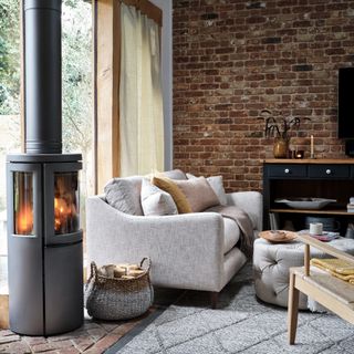 A cosy living room with an exposed brick wall, a light grey sofa and a lit wood-burning stove next to it