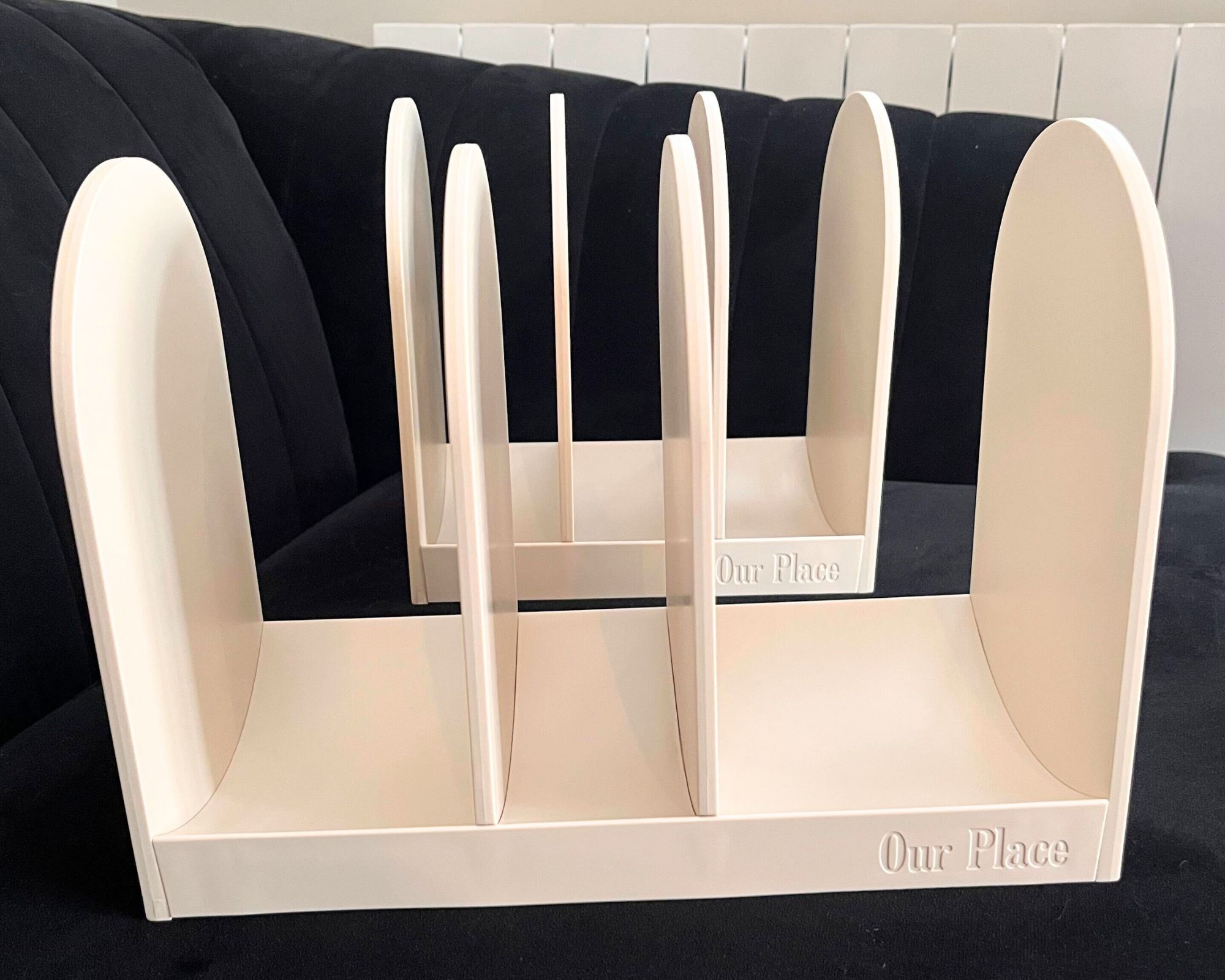 The put-together matte cream pan organizer of the Our Place 11-Piece Essentials Cookware Set. There are two, each has three sections. They are pictures on a black sofa