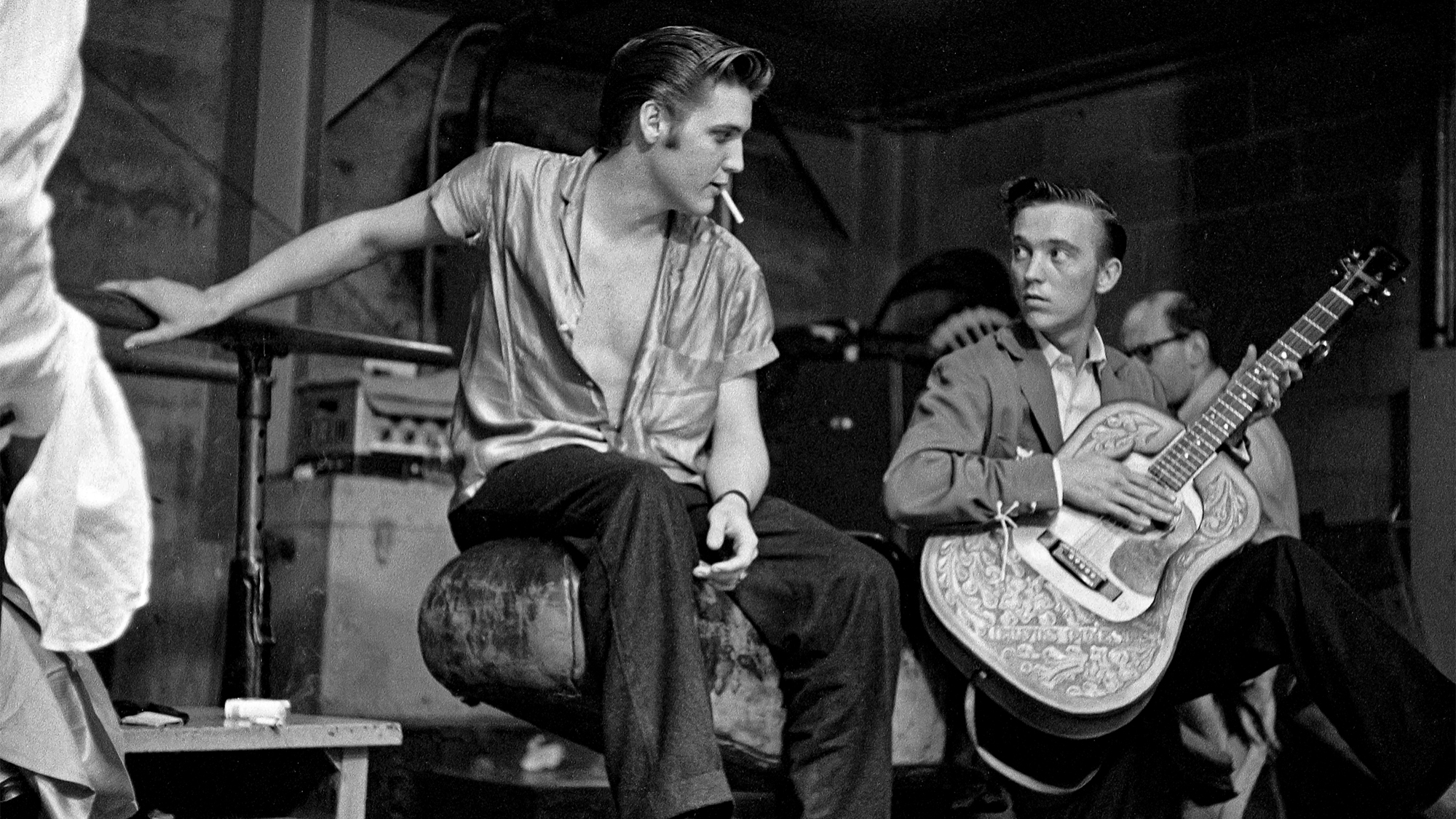 Elvis Presley, Scotty Moore, and Gene Smith backstage at the University of Dayton Fieldhouse, May 27, 1956. Photographer Marvin Israel is partially visible in the background.