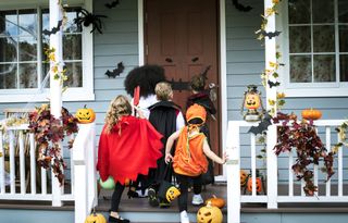 Four children dressed up in Halloween costumes while trick or treating together.
