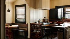 Image of a kitchen drenched in yellow panelling. There is black trim around the windows and darkwood on the countertops