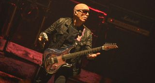 Joe Satriani wields a power drill onstage as he performs Poundcake with Sammy Hagar. Satch wears dark shades and his drill is chrome to match the finish on his Ibanez signature guitar 'Chrome Boy'