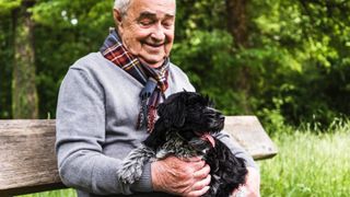 Man sitting on park bench cuddling small black dog