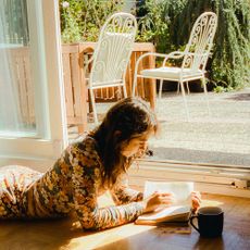 Woman laying on floor reading book on sunlight in her cozy house with patio