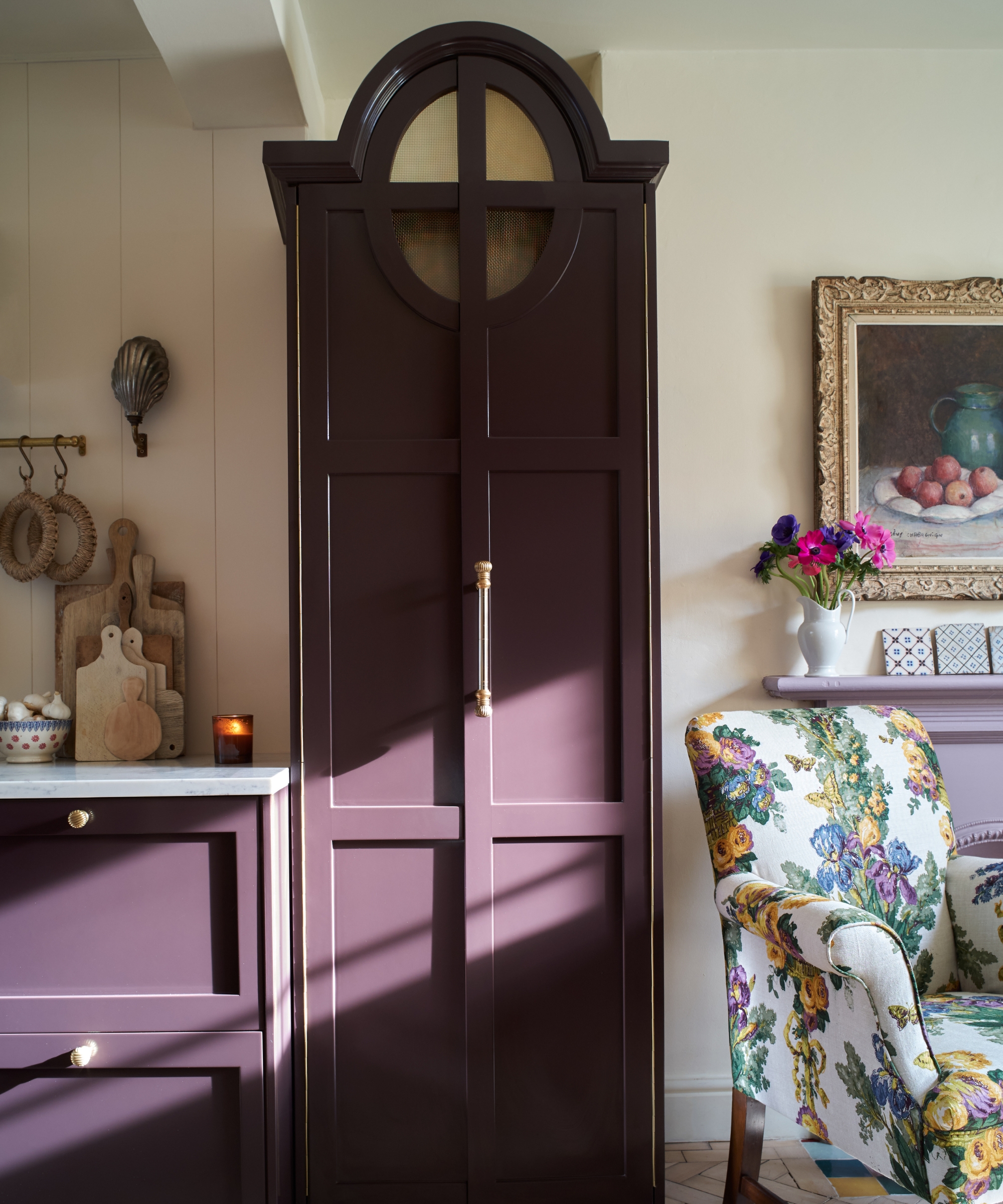 The corner of a small kitchen with warm white walls and aubergine cabinetry