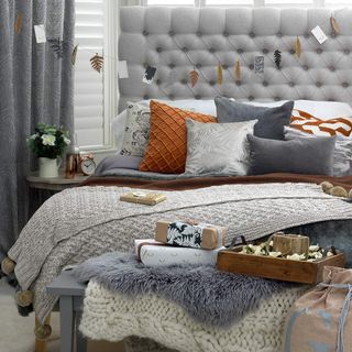 Grey headboard of bed layered with cushions and blankets