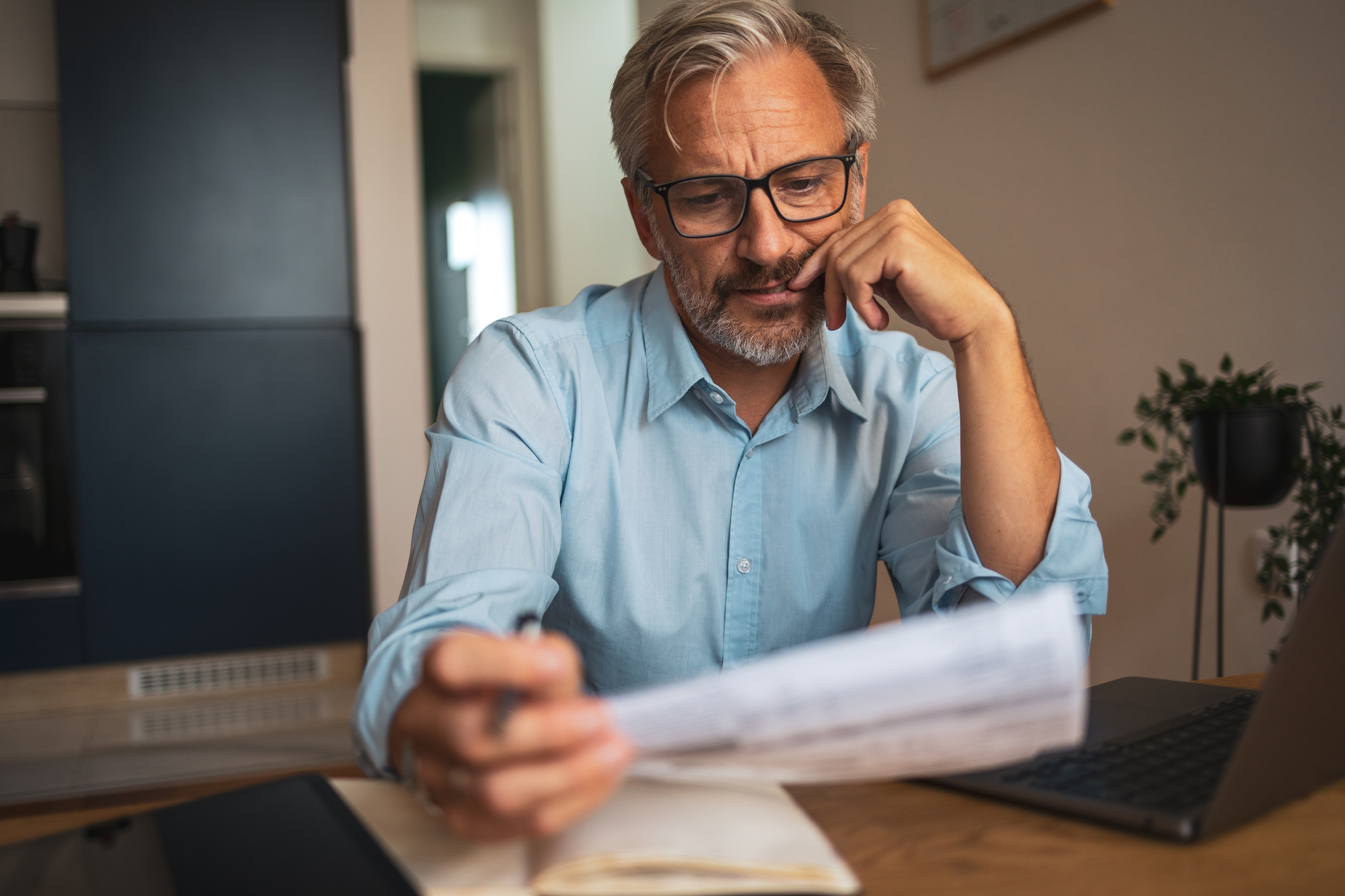 Mature man reviewing financial statements at home using laptop.