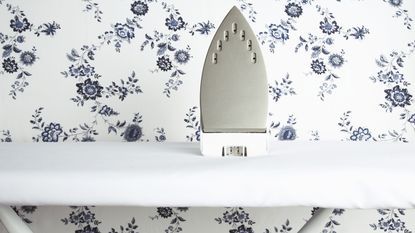 A dry iron on white ironing board with blue and white floral wallpaper wallcovering wall decor in background