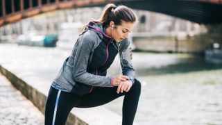 Woman pausing beside canal to check sports watch