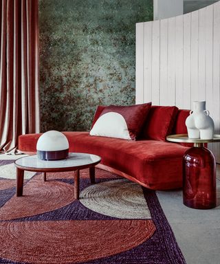 Apartment living room ideas with a red and purple curved-print rug, curved red chaise longue and green patterned walls.