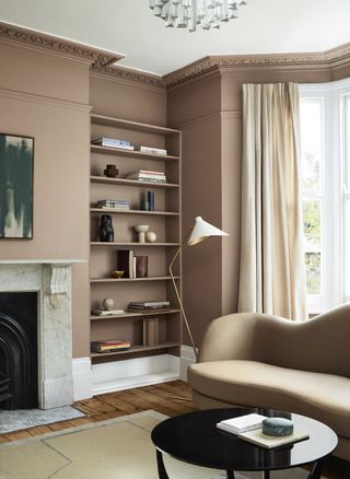 living room with earthy tones, brown couch, bookcase, drapes