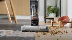 Bissell Crosswave OmniForce Edge wet dry vacuum pictured behind spilled pet food and food, positioned on line between wooden and laminate floors.