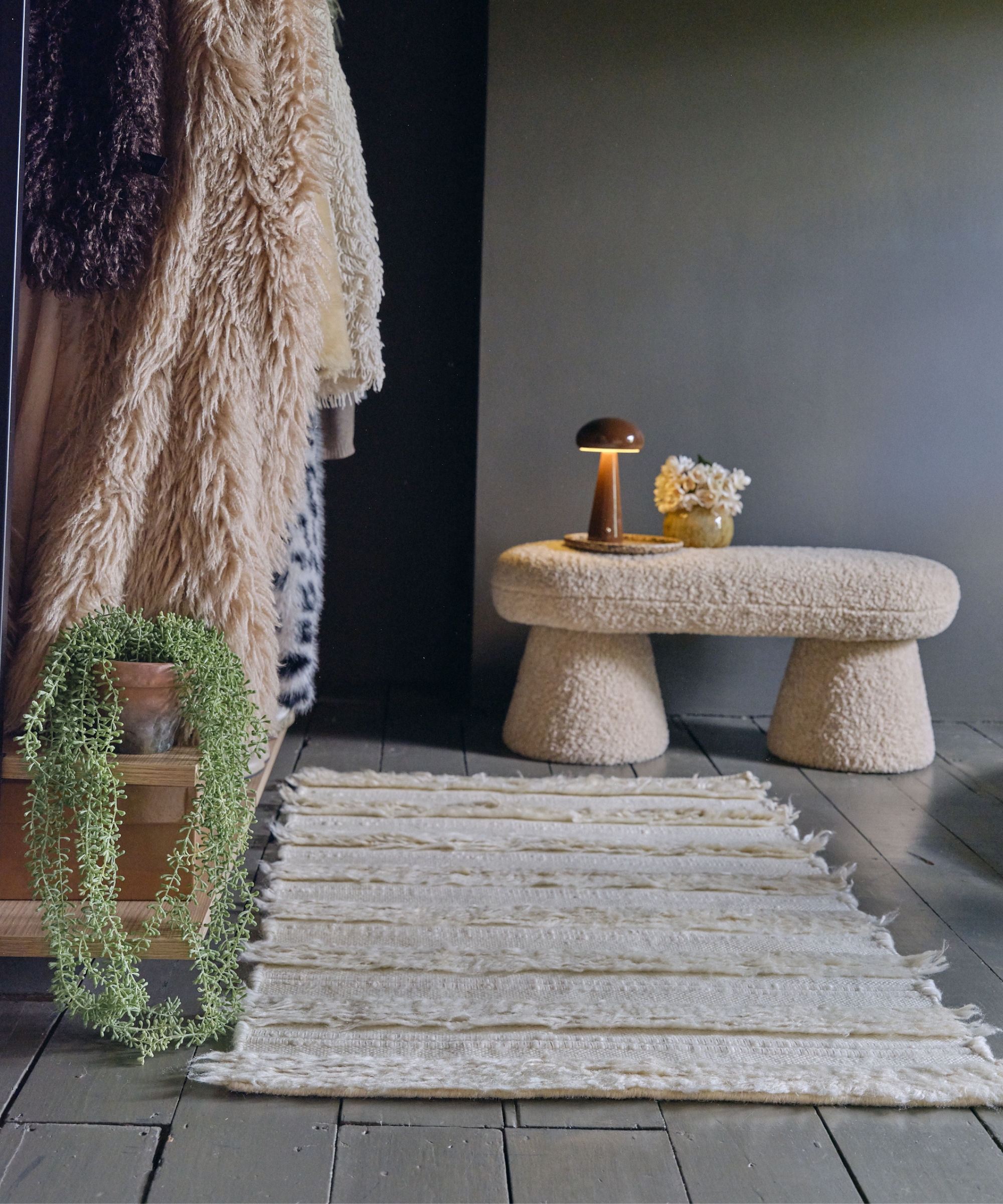 Boucle mushroom-shaped bench with a lit lamp and flowers, faux fur throws and a fringed rug nearby.