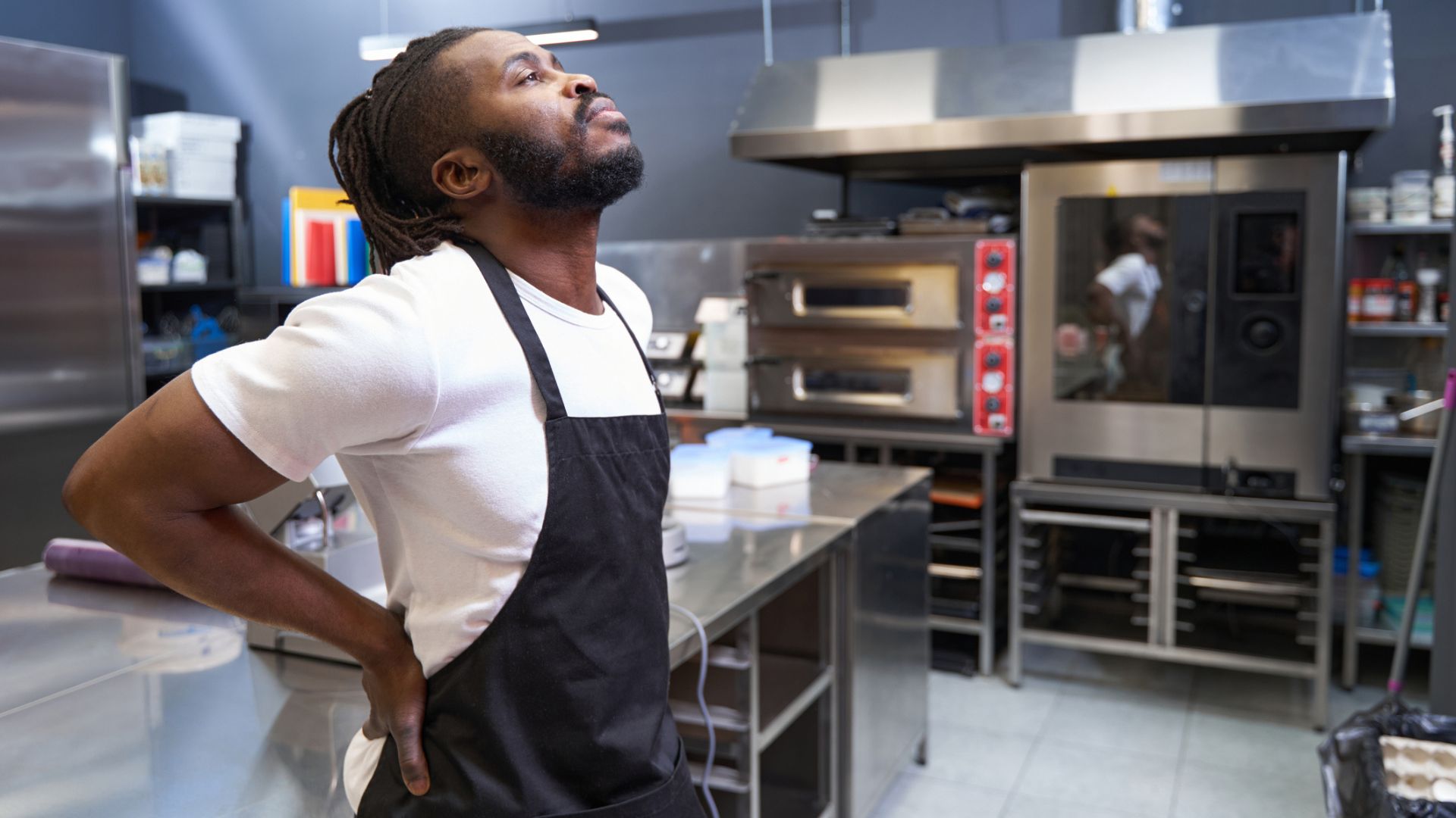 chef in kitchen holds sore back after being on his feet all day