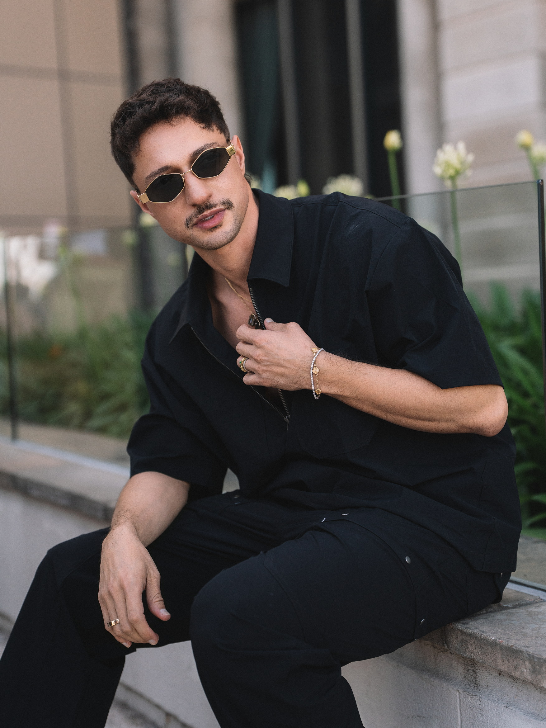 a white man in an all-black outfit with dark sunglasses and dark hair