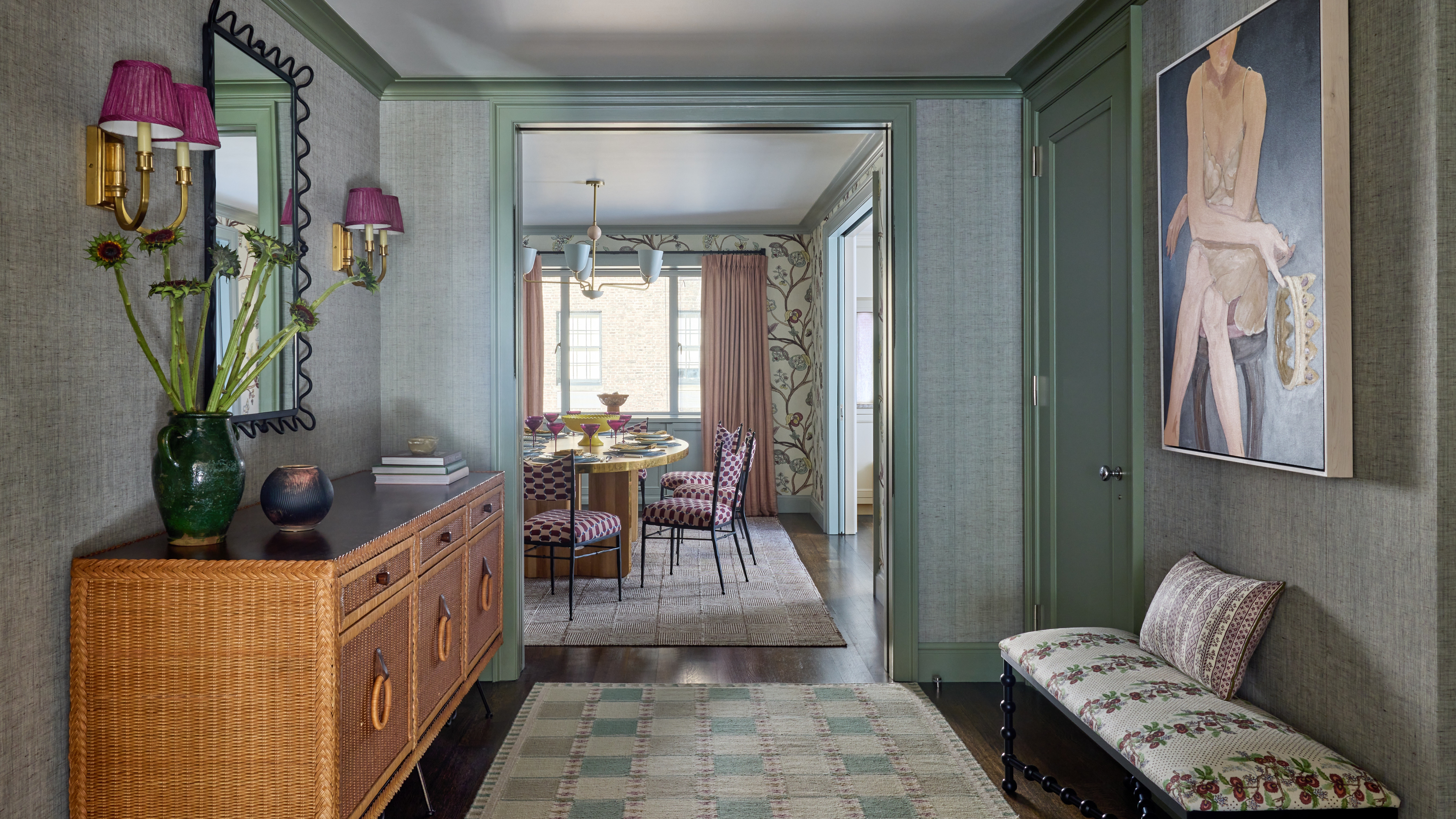 Upper East Side apartment entryway with green-painted joinery, wicker credenza, grasscloth walls, patterned bench and sage kilim runner.