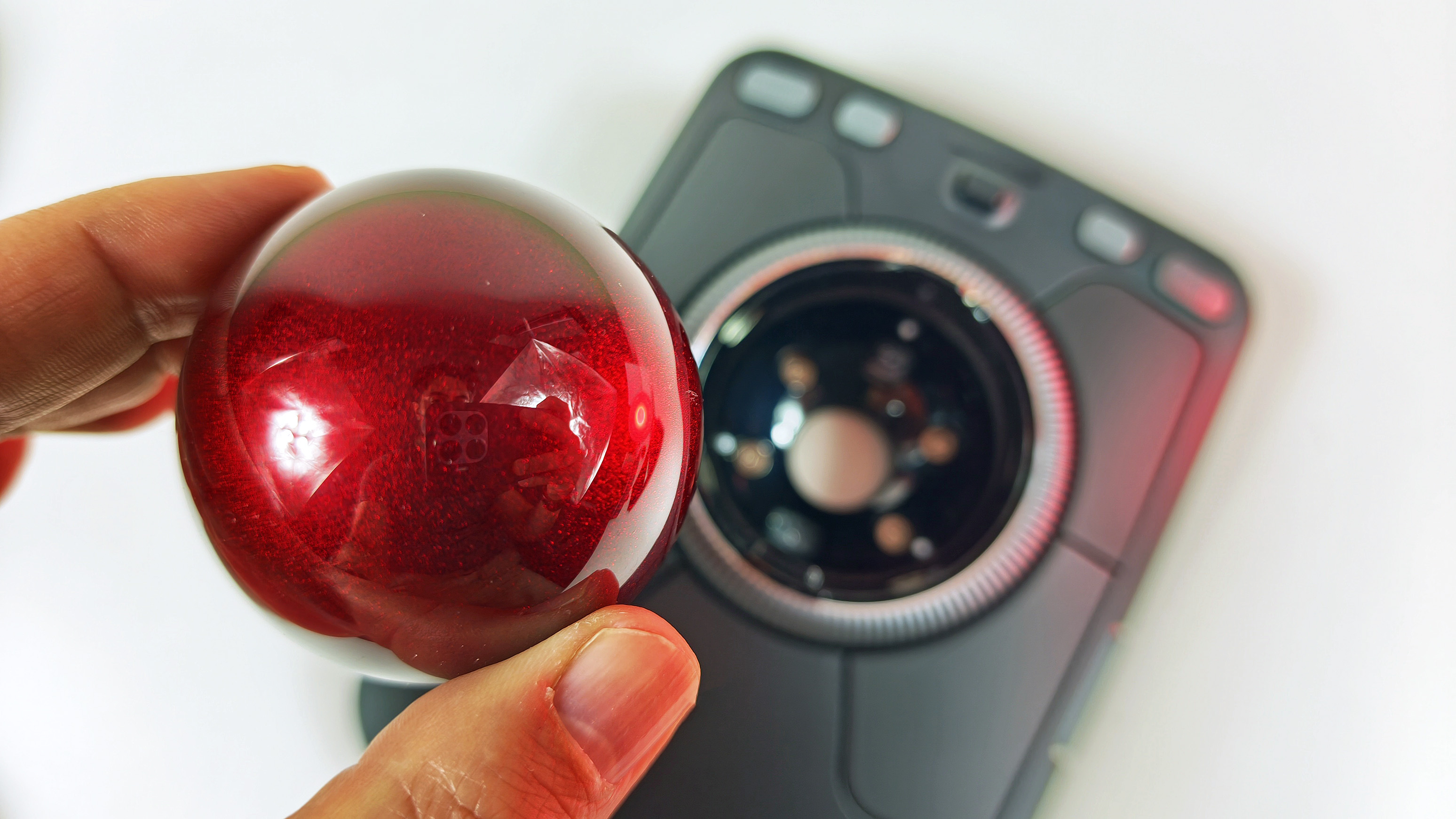 A hand holding the removable 55mm glossy red sphere above the open tracking socket of the Kensington Expert Mouse Pro TB900 EQ trackball.