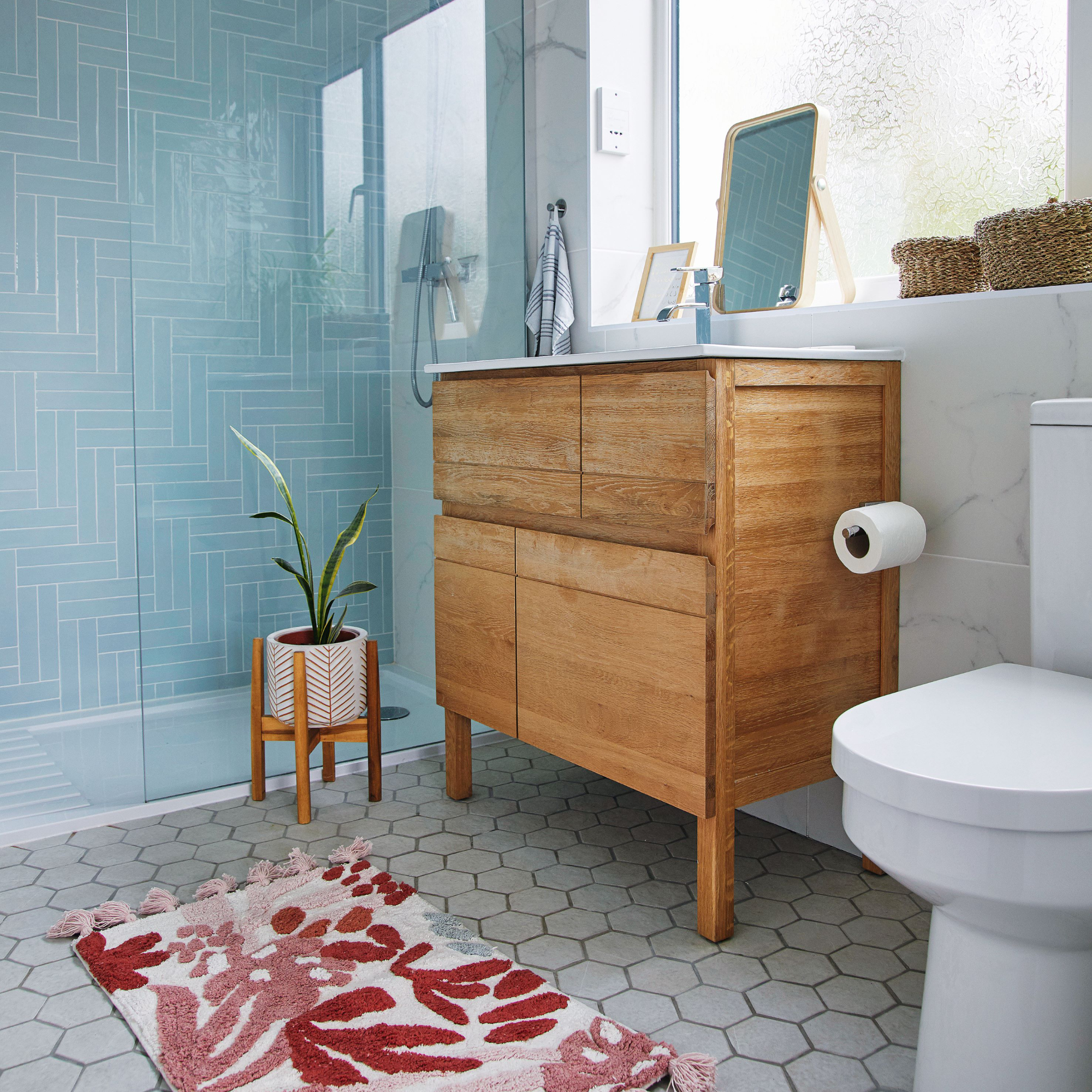 Blue and marble tiled bathroom walls with tiled floor, pink bath mat and wooden sink