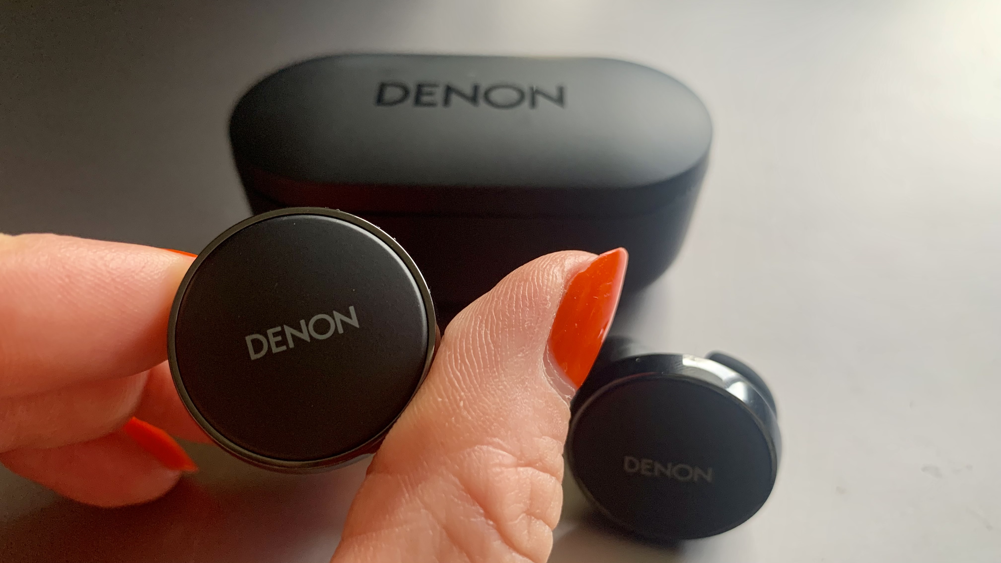 Denon PerL Pro earbuds held in a woman's hand, with the case behind.