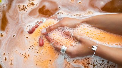 Orange bubbling bomb of bath dissolving in hands in silver accessories. Ayurveda bomb for the bath