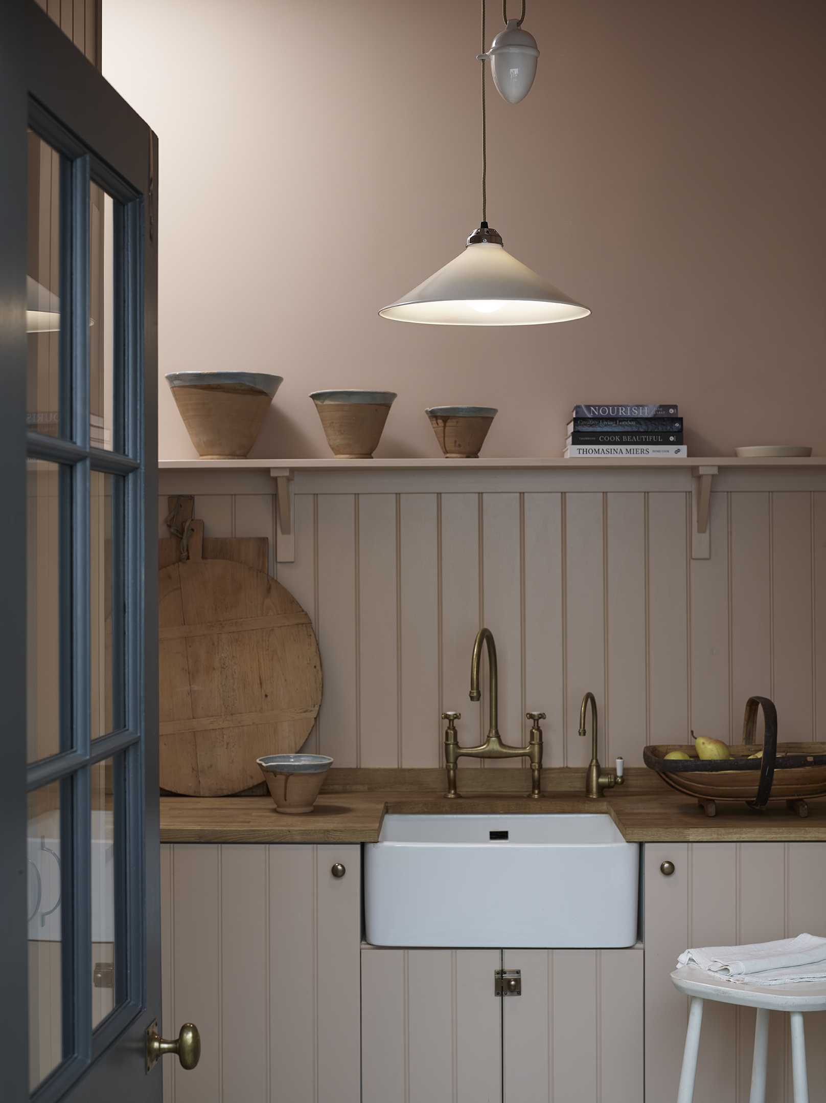 A pink kitchen with a belfast sink and a pendant light