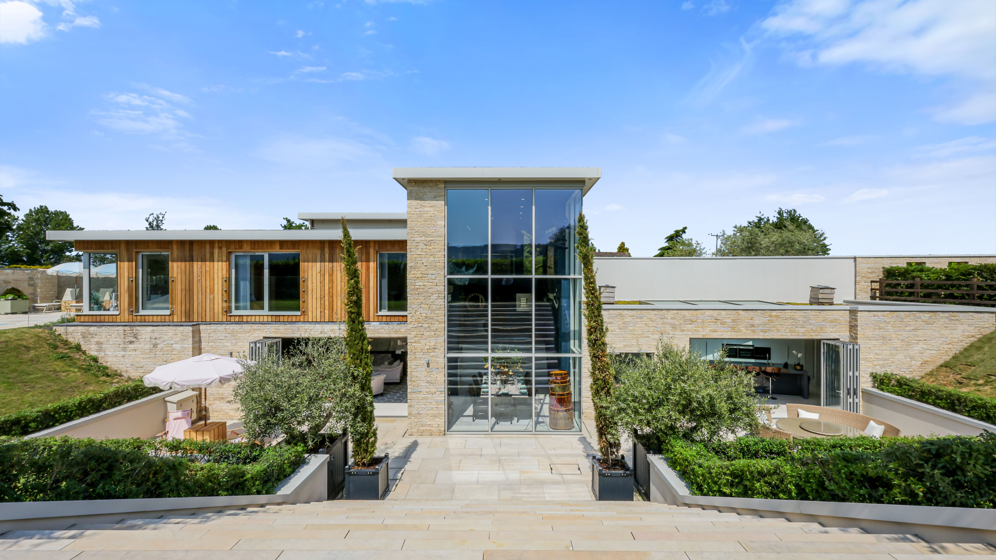 modern self-build house with double height glass fronted entrance with remainder of exterior clad in stone and wood