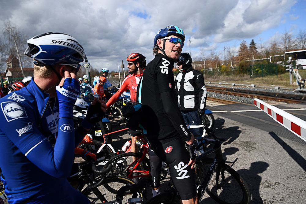 Riders wait for a train to pass during stage 4 at Paris-Nice