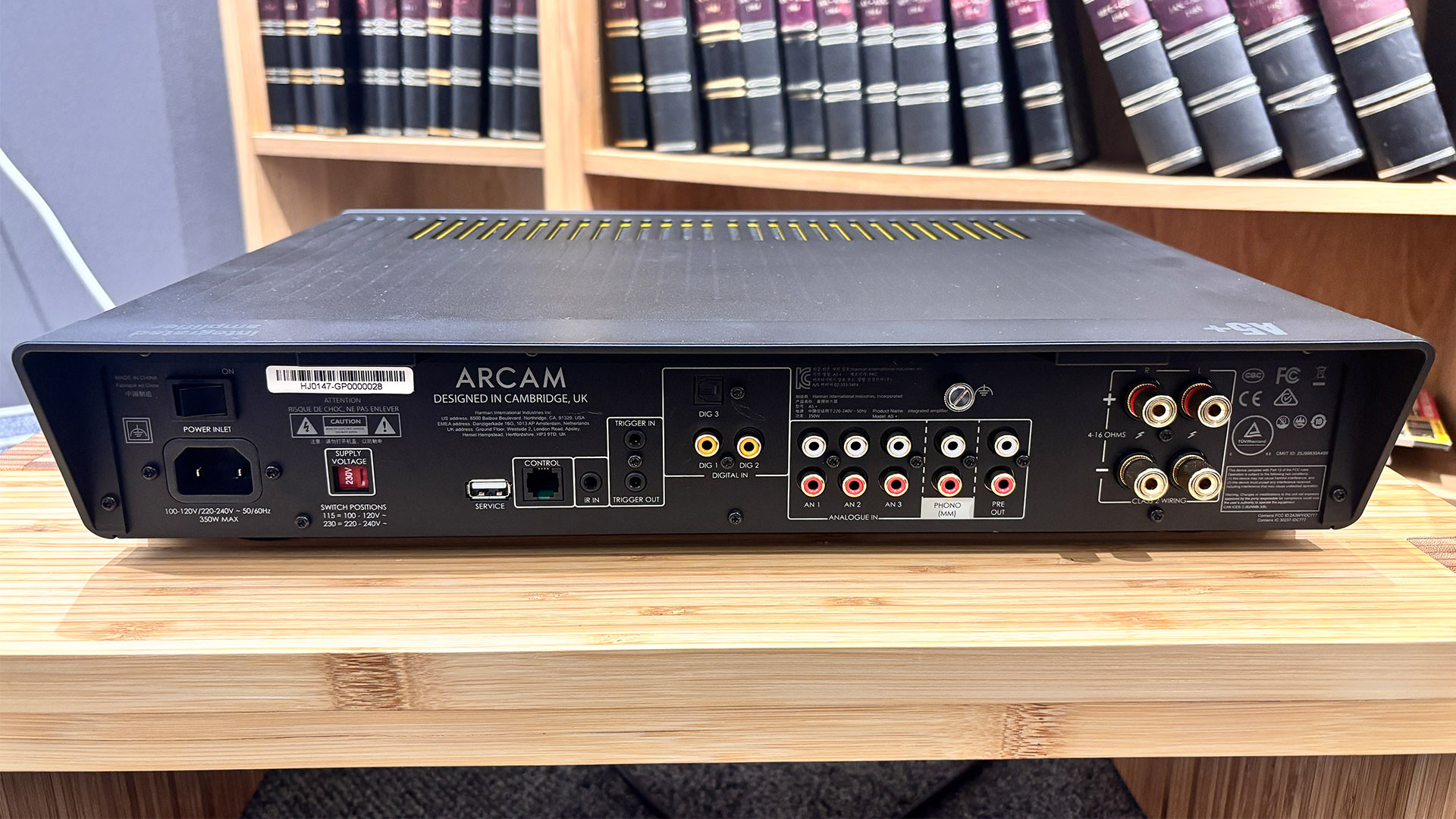 Arcam A5+ integrated amplifier on wooden hi-fi rack in front of bookcase, rear of unit showing connections