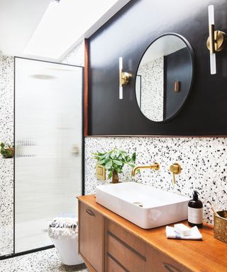Terrazzo tile covered bathroom with black walls and smart wall lights hanging above a vanity unit