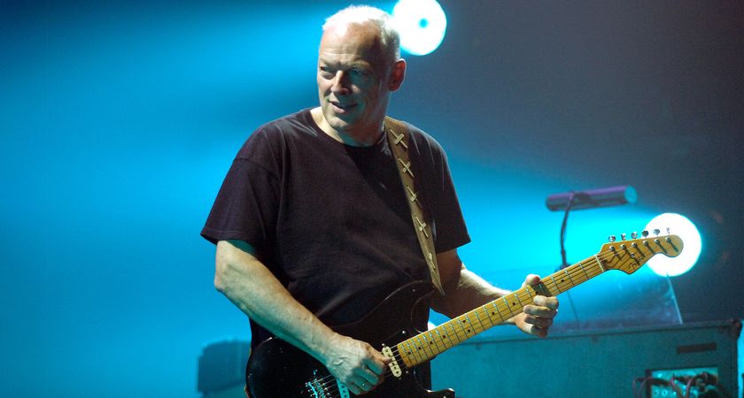 David Gilmour is bathed in blue stage lights as he performs with a black Stratocaster.