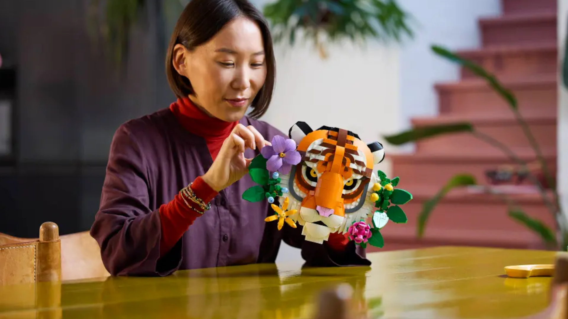 A woman places the final pieces on the Lego Fauna Collection - Tiger set while sat at a wooden table