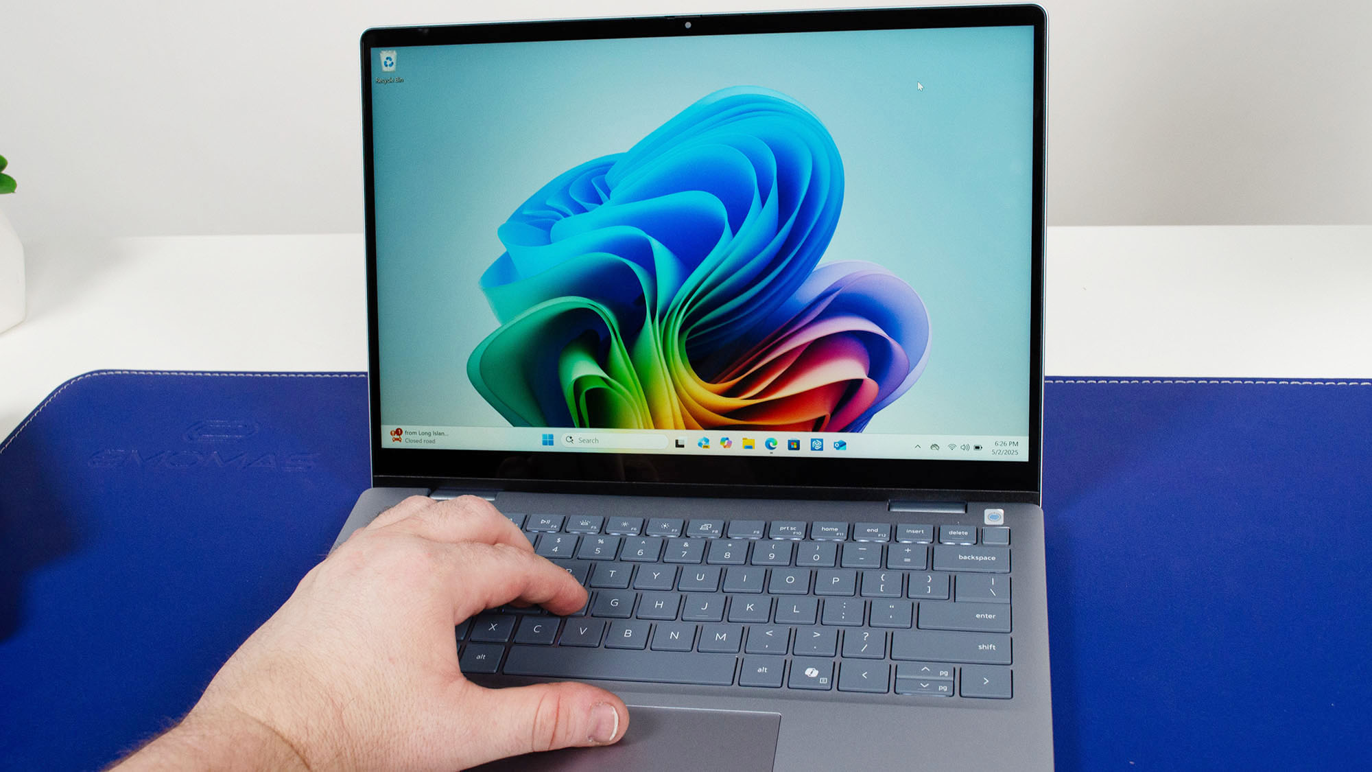 A masculine hand resting on the keyboard and trackpad of the Dell 14 Plus 2-in-1