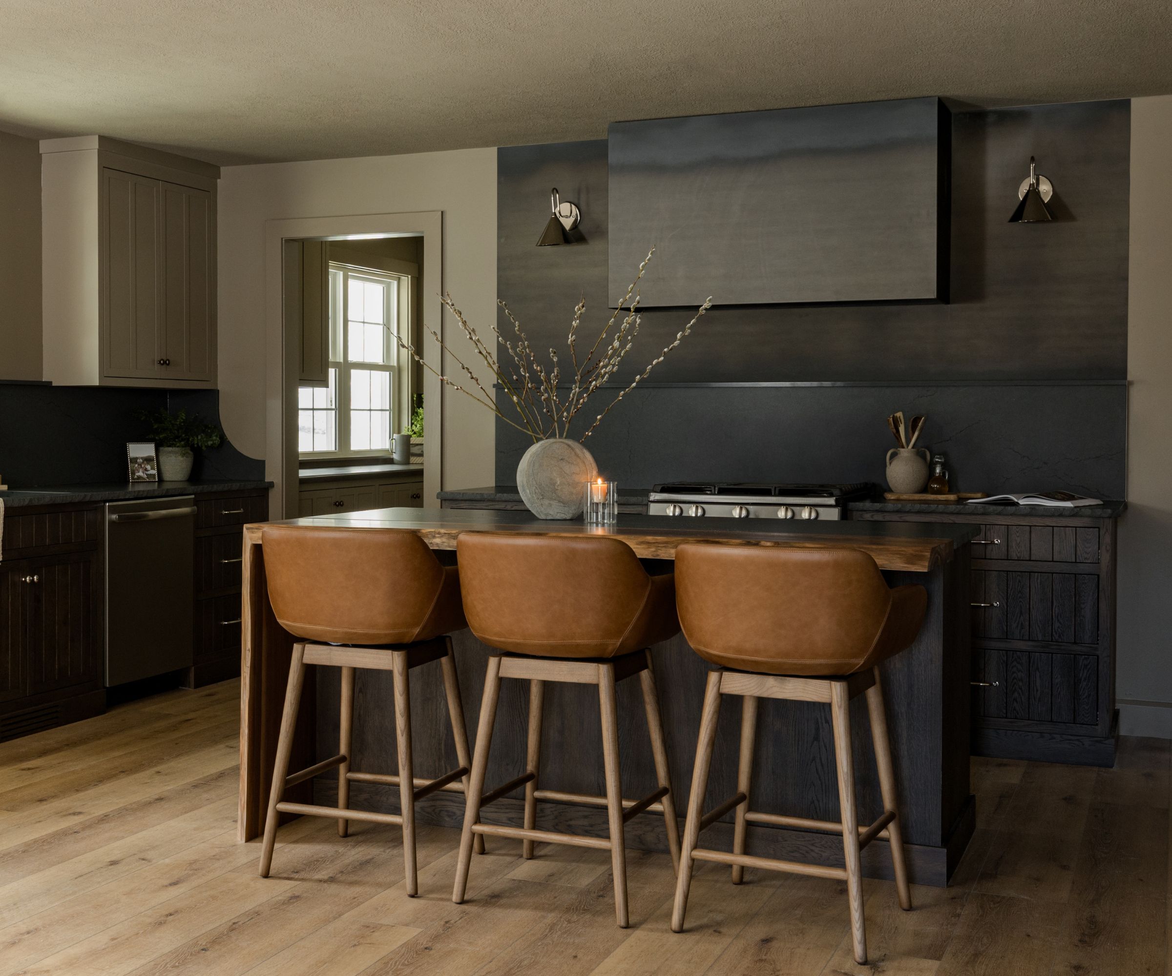 A black kitchen with an 18 inch slab backsplash and brown leather bar stools