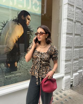 Influencer wears a leopard print top, black pants, a burgundy bag, a chain necklace, and sunglasses.