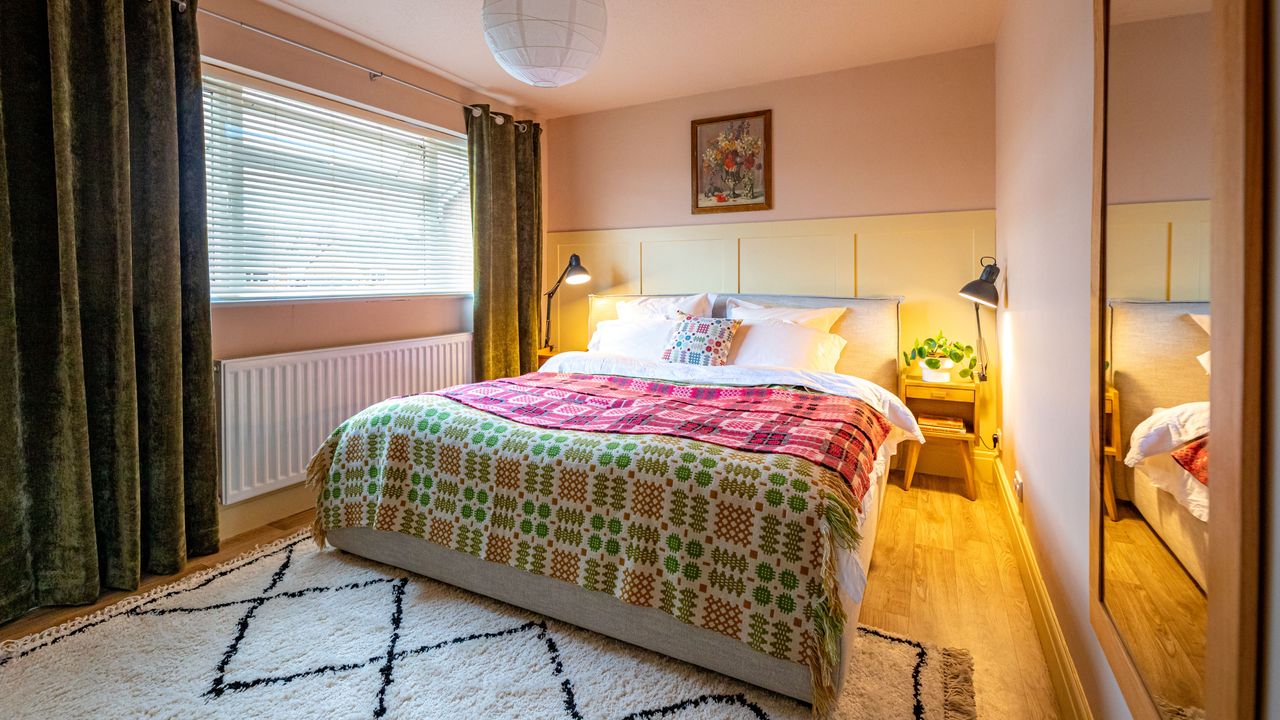 Bedroom with double bed and colourful blankets, bedside tables and lamps, green curtains