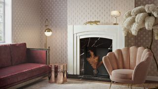 A lounge with a fireplace, sofa and velvet chair that's been wallpapered using a pink and gold art deco wallpaper