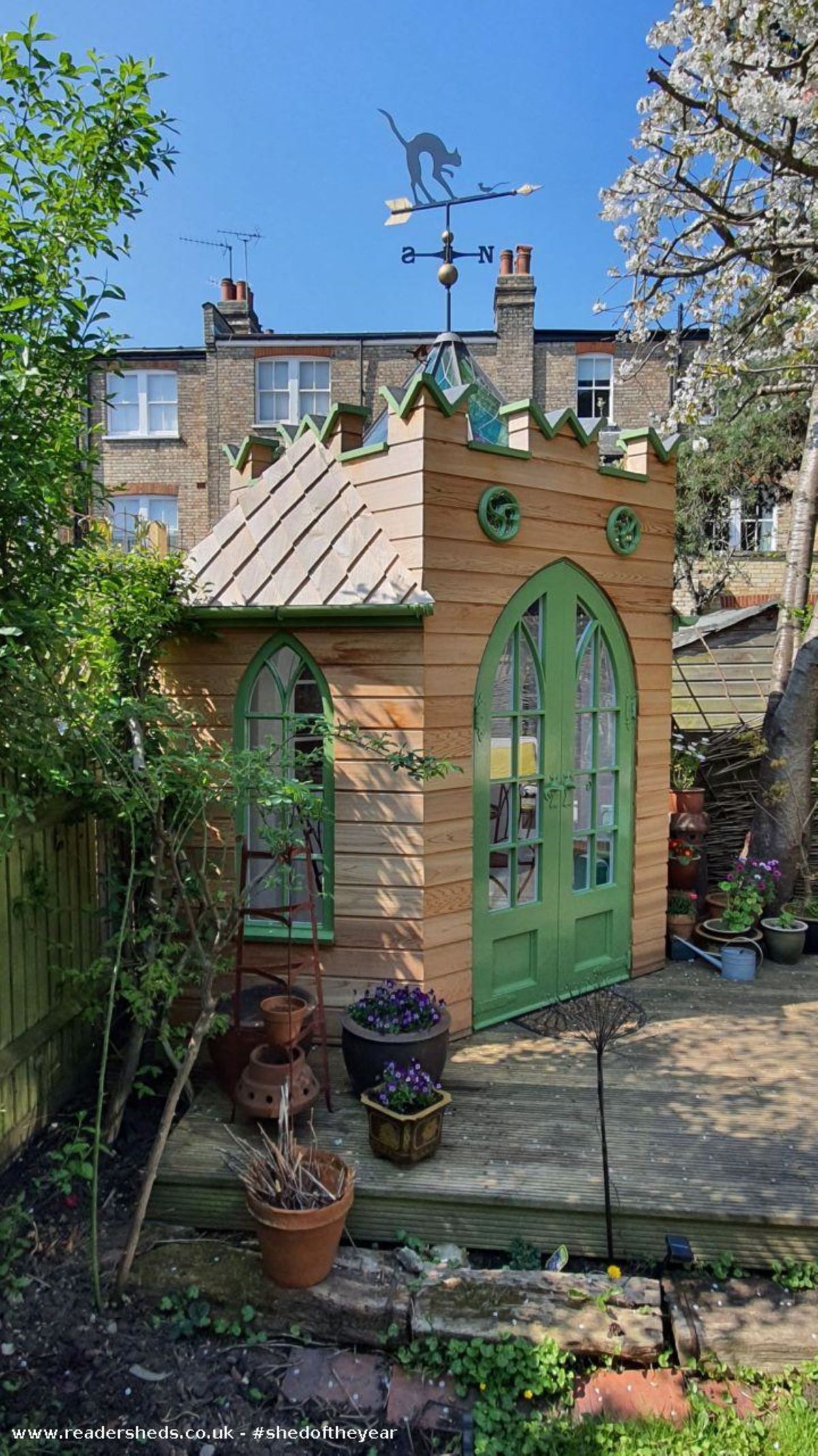 This shows a small wooded shed with green doors with bushy surroundings encircling a tiny shed