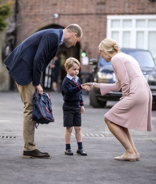 Prince William with his son Prince George, who is dressed in school uniform on his first day of school at Thomas's Battersea. Prince George is nervously shaking his teacher's hand.