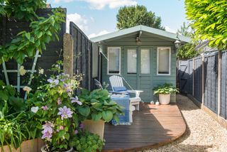 Modern garden ideas: green painted shed with decked area and white chairs outside
