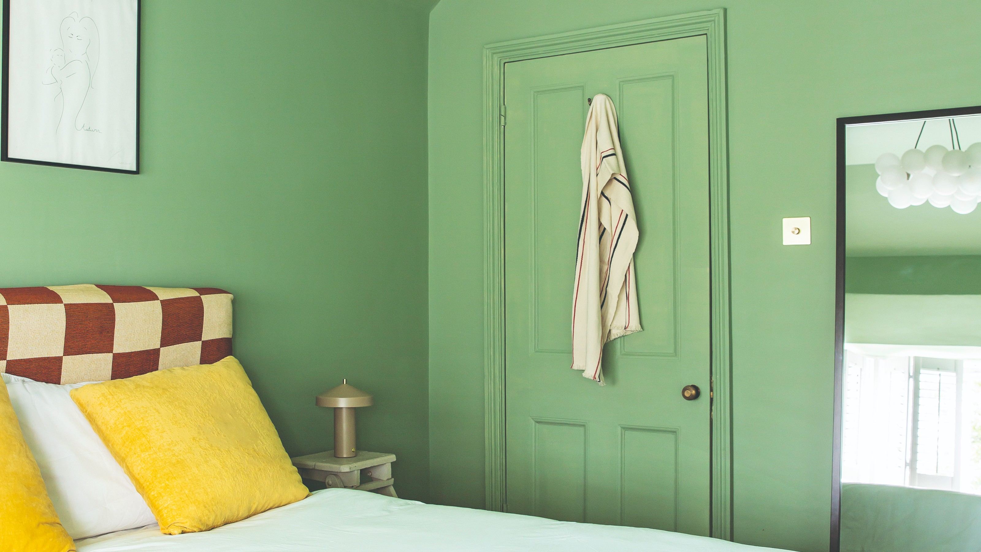 A colour-drenched green bedroom with a chequered headboard and bright yellow cushions on the bed