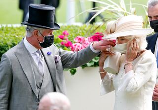 Prince Charles, Prince of Wales helps Camilla, Duchess of Cornwall put on her face mask as they attend day 2 of Royal Ascot